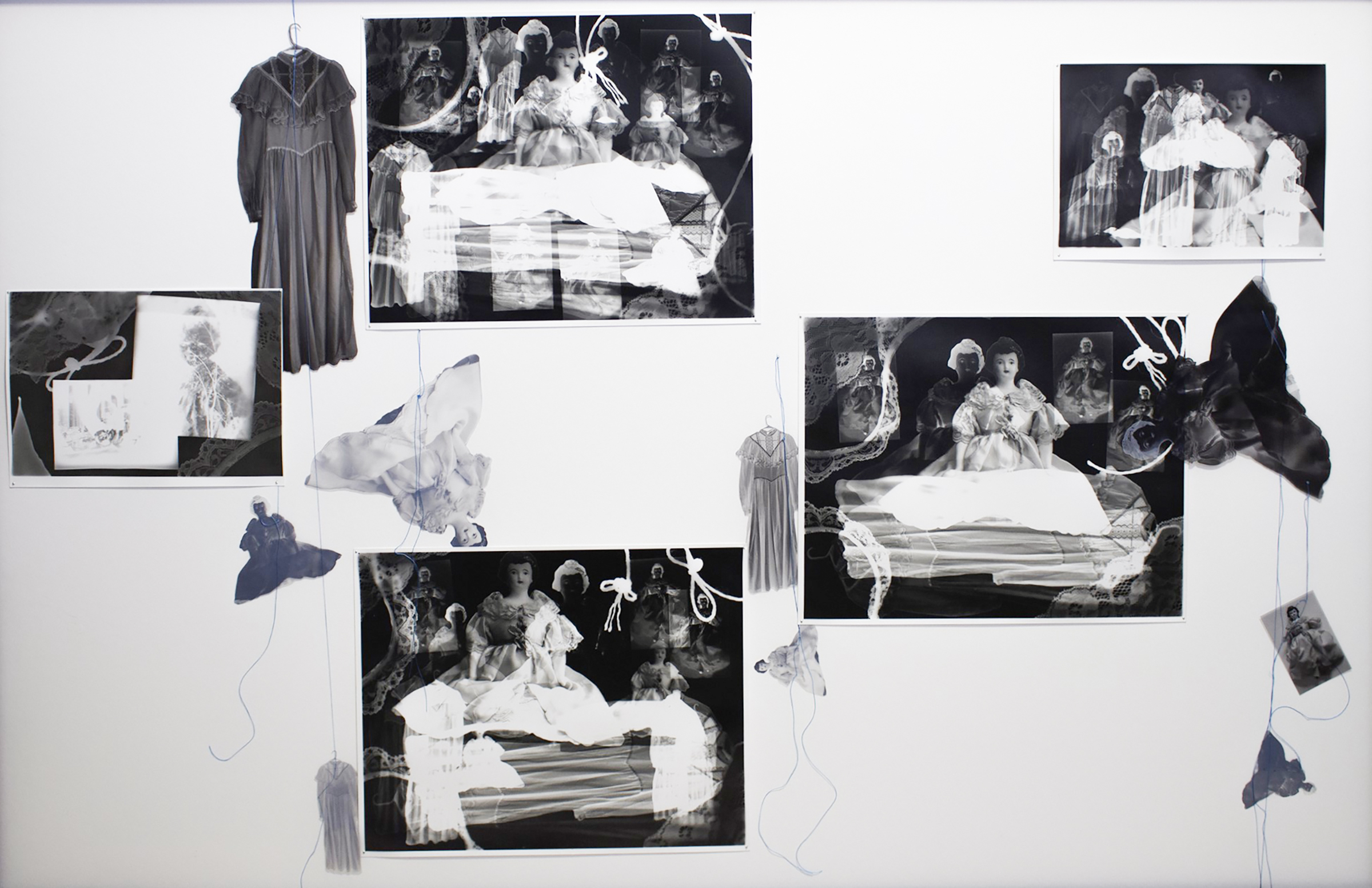 Series of black and white gelatin silver photograms arranged in one composition. Imagery consists of various sizes, both positive and negative, of dolls, dresses, and a boy, with white silhouettes of lace and fabric overlaid and surrounding them. Imagery overlaps and blends into one another. Outside of the photograms, transparent images of dolls and dresses hangs from blue thread.